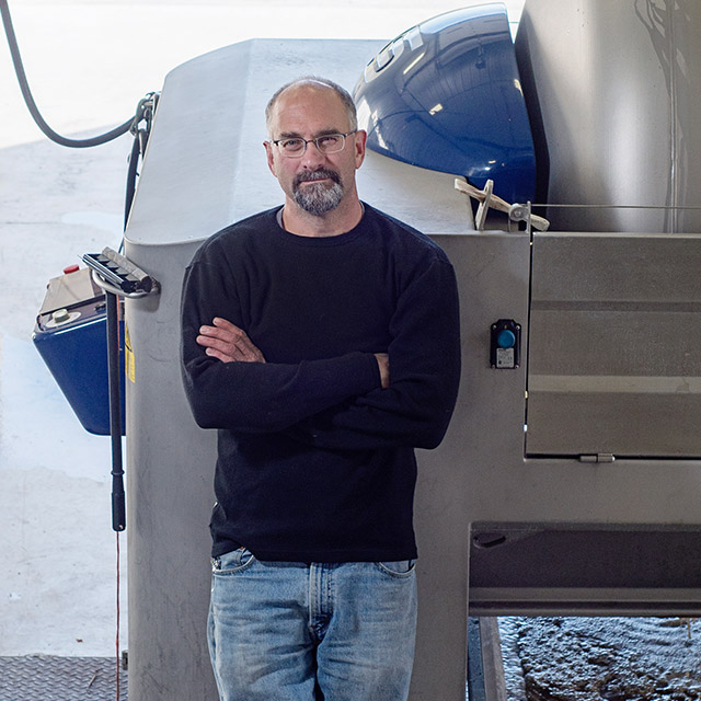 Chris Stamp leaning against winery equipment